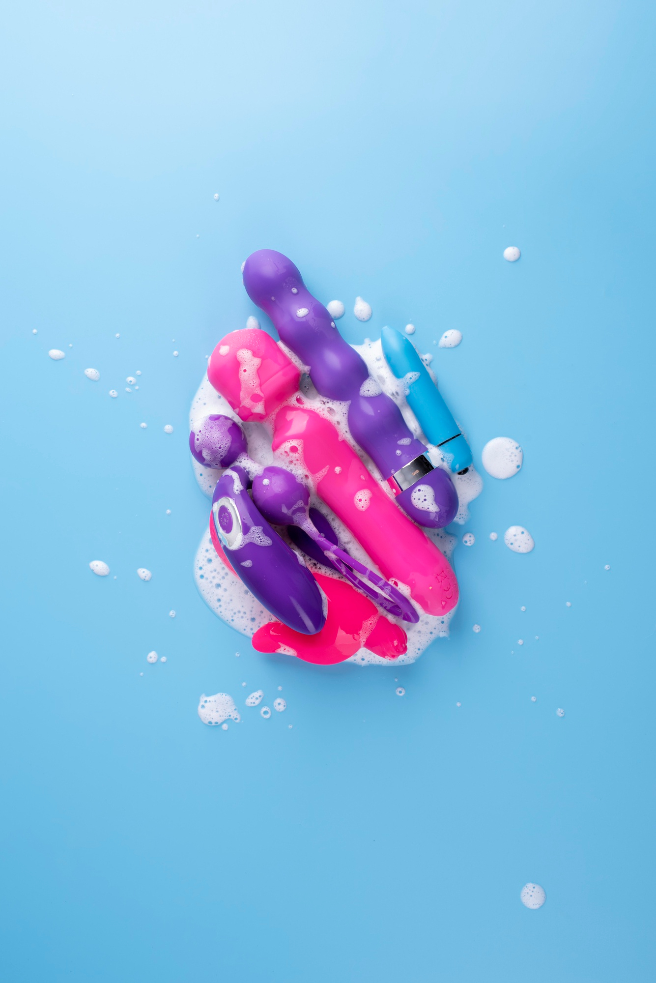 A big variety of sex toys covered in lather on a blue background.