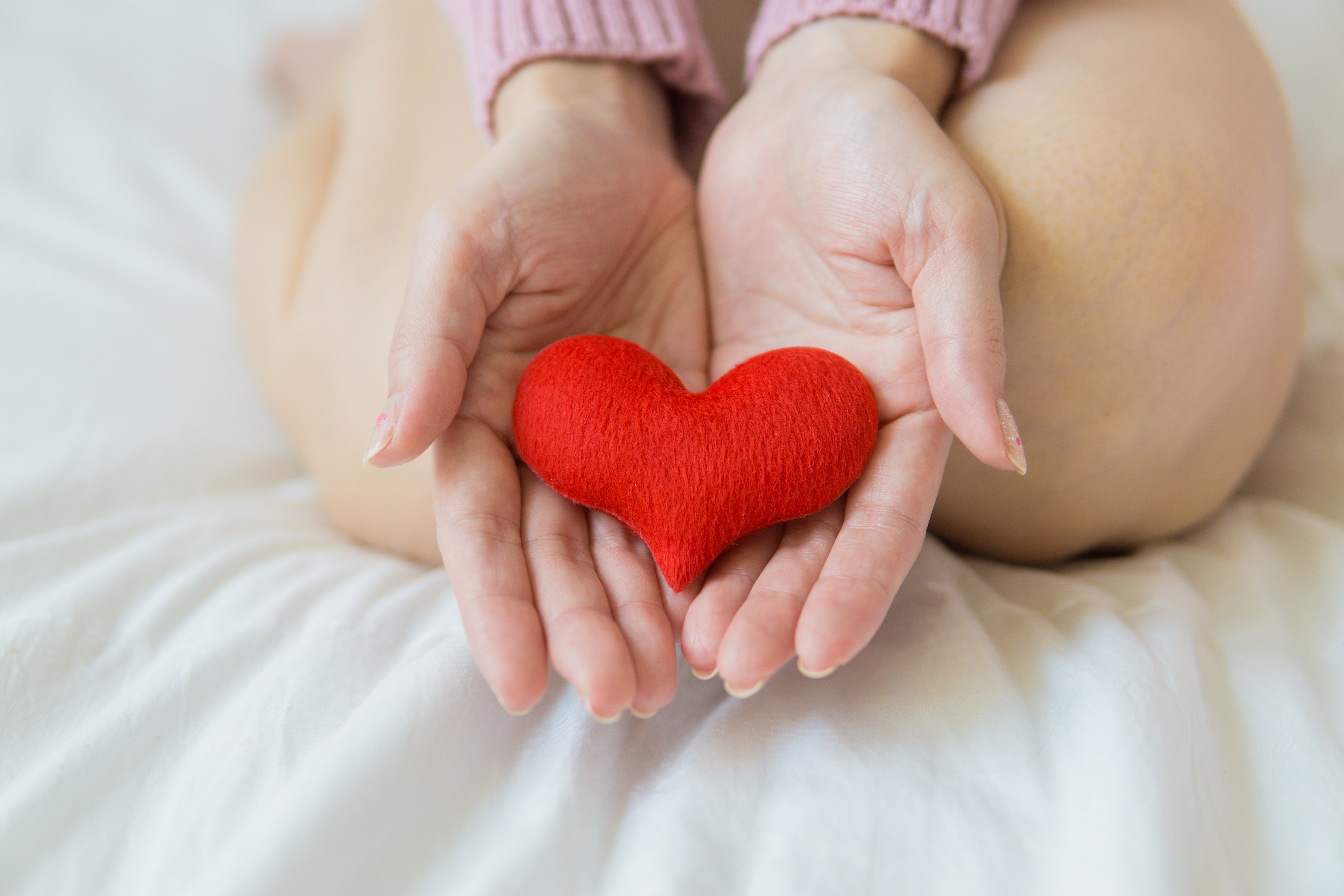 An image with a person on the bed with a wool heart in their palms.
