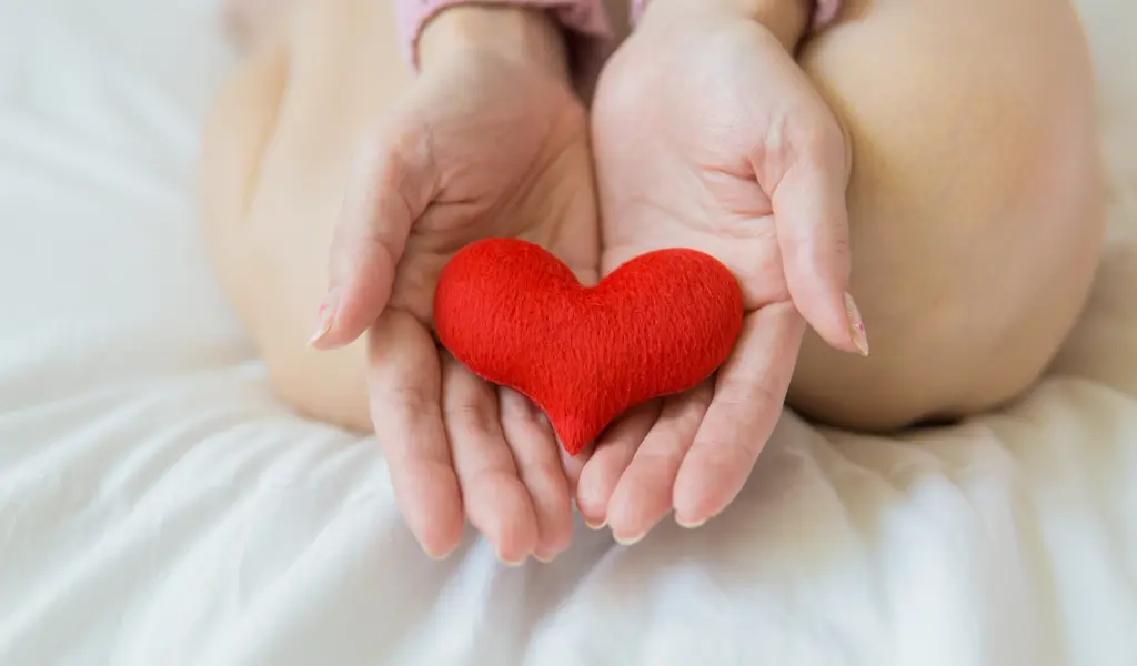An image with a person on the bed with a wool heart in their palms.